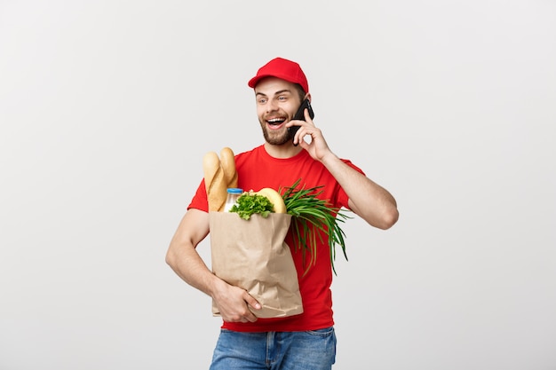 Handsome grocery delivery man talking to mobile and holding grocery paper bag.