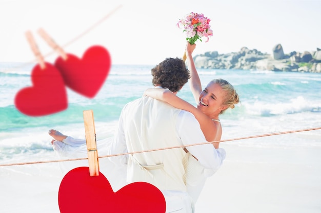 Handsome groom carrying his beautiful laughing wife against hearts hanging on a line