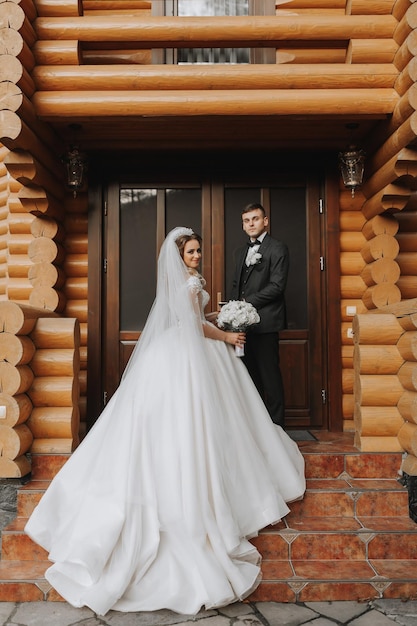 Handsome groom and charming bride stay together near modern wooden house in park