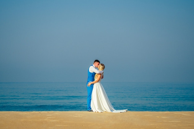 Sposo bello in un vestito elegante e una bella sposa in un abito da sposa sulla spiaggia. concetto di una cerimonia di matrimonio chic e ricca sulla spiaggia. copyspace