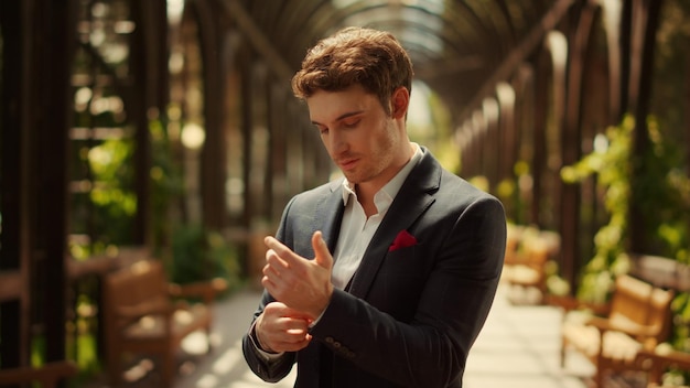 Handsome groom looking at camera under arch Man buttoning up shirt in park