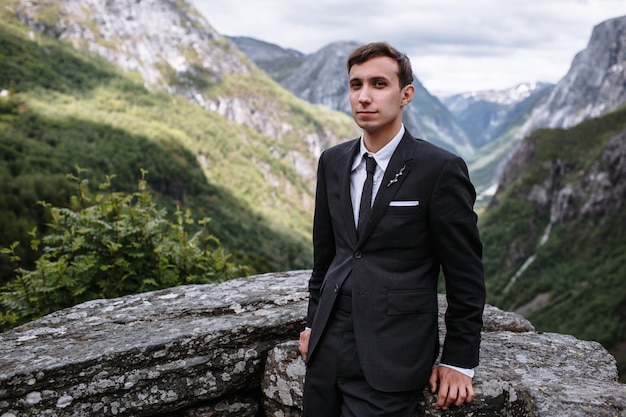 Handsome groom in a suit next to a stone wall