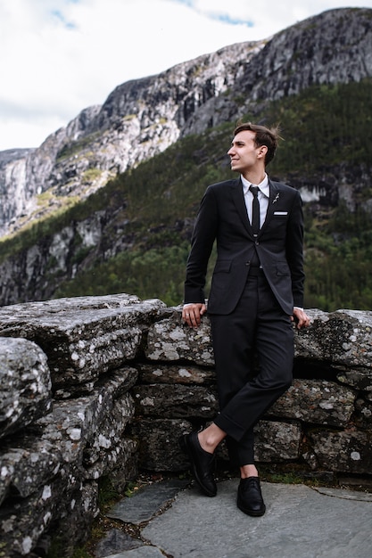 Handsome groom in a suit next to a stone wall