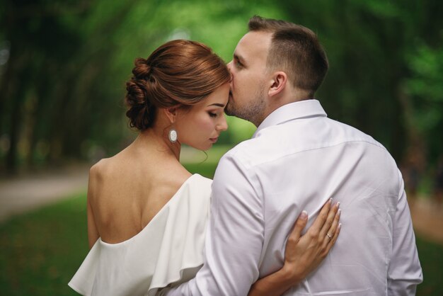 Handsome groom tenderly kissing his beautiful wife on a walk in the park