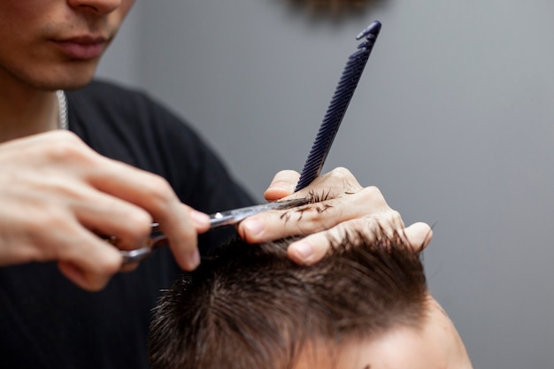 Photo handsome guy get a haircut at the hairdresser, kazakh hairdresser cuts manually with scissors and a comb, short haircut close-up