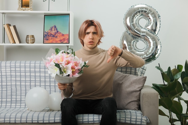 Handsome guy on happy women day holding bouquet sitting on sofa in living room