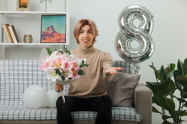 handsome guy on happy women day holding bouquet sitting on sofa in living room