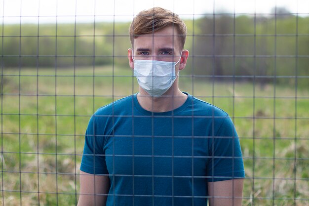 Handsome guy in protective mask on his face isolated standing behind bars, lattice. Restriction of freedom. Self isolation because of coronavirus epidemic virus infection. Covid-19. Isolated young man