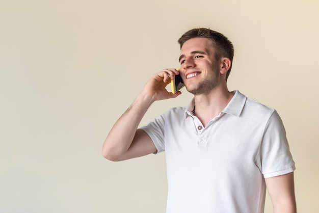 Handsome guy talking on the mobile phone and smiling on the beige background