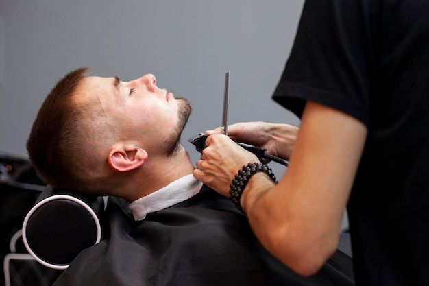 ハンサムな男は、理髪店のクローズ アップで短いひげを剃るトリマーでひげをトリミングしました。