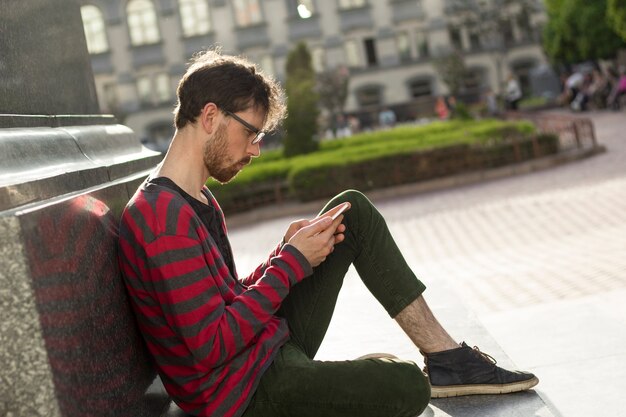 Handsome guy uses a smartphone outdoors.