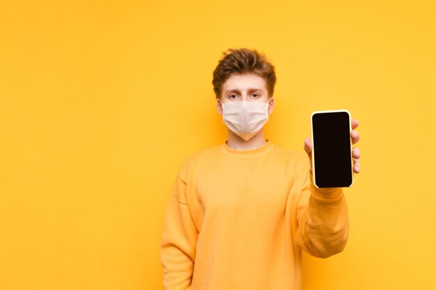 Handsome guy in a yellow sweatshirt and a protective gauze mask stands on an orange background