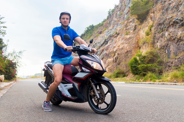 Handsome guy, young man, biker or motorcyclist  is riding, driving motorcycle, moped or bike, . Rider  in helmet on the road in mountains in a summer day in Asia, Vietnam