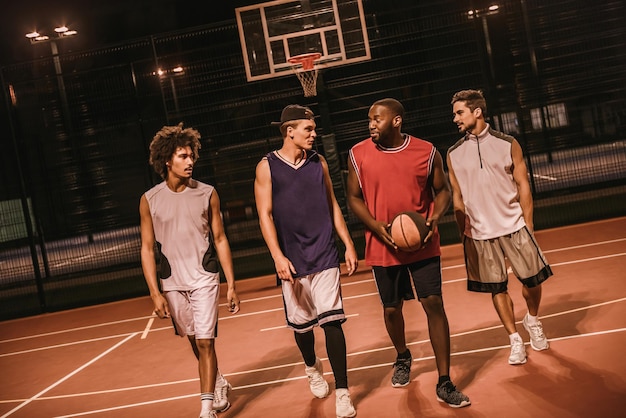 Handsome guys are playing basketball outdoors at night