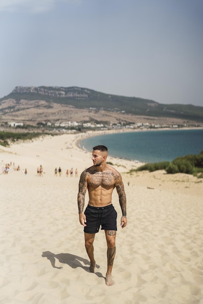 Handsome halfnaked caucasian man walking on the sand enjoying his vacation