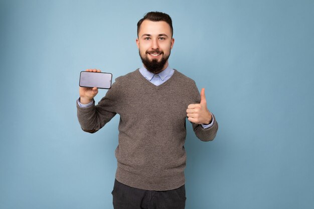 Handsome happy cool young brunette unshaven man with beardwearing stylish grey sweater and blue