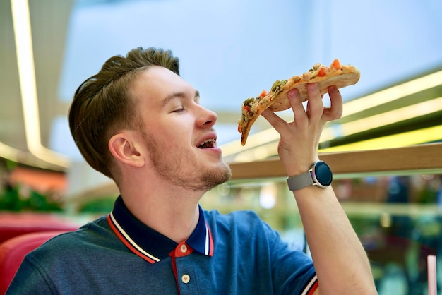 Handsome happy guy, young man is eating biting slice of tasty pizza, Italian food