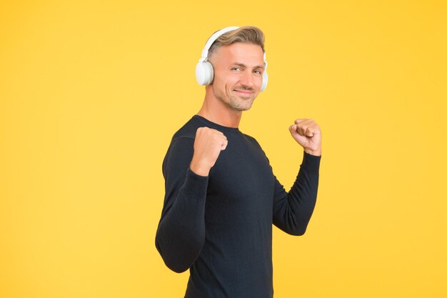 Handsome happy male with nice smile demonstrate high quality headset being in good mood while listening music online techno shop