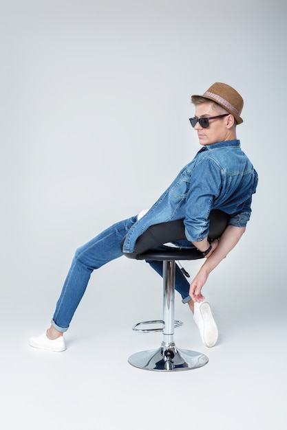 Handsome happy  man in denim and sunglasses sits on chair