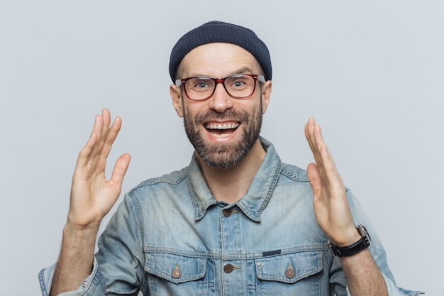 Handsome happy man raises hands with excitement, has overjoyed expression