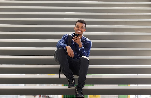 Handsome happy man sitting on stairs using smart phone