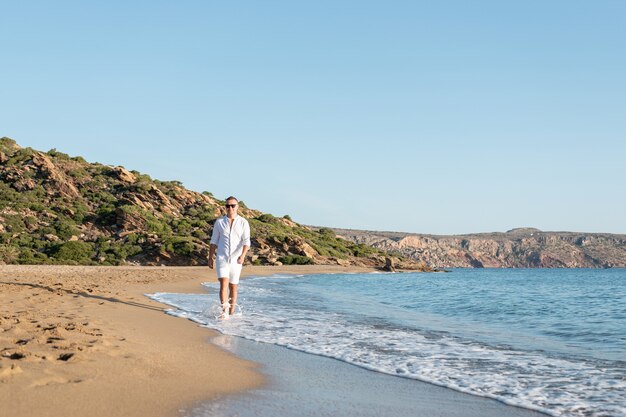 Handsome happy man in white shirt walking on the beach.