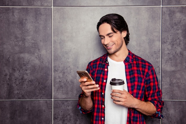 Handsome happy man with cup of coffee reading sms on phone