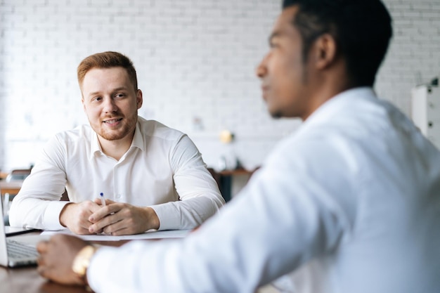 Handsome happy young business man explaining to African partner the benefits of new deal to colleague or client Businessman holding conversation with business client