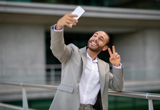屋外でスマートフォンで自撮りをするハンサムな幸せな青年実業家