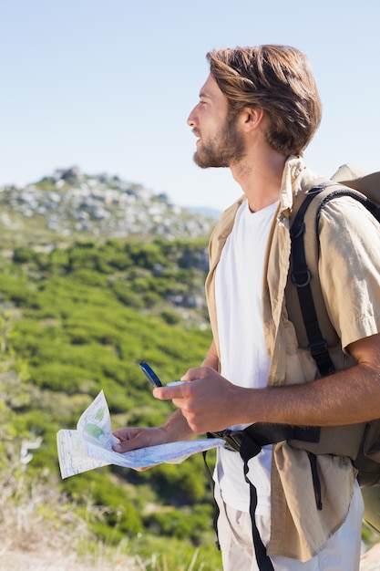 Handsome hiker holding map and compass at mountain summit