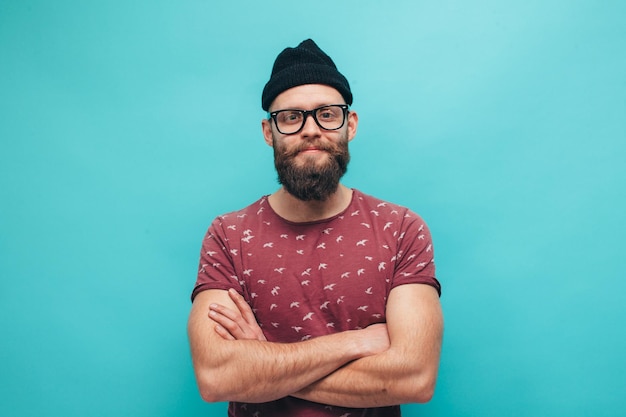 Handsome hipster guy with beard smiling happily dressed casually with black beanie on head isolated over a blue studio background The concept of people crazy emotions