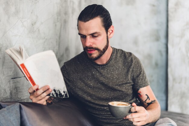 Uomo bello hipster rilassante leggere lo studio di lavoro del libro di carta e guardare la rivista della pagina mentre era seduto sulla sedia in bar e ristorante