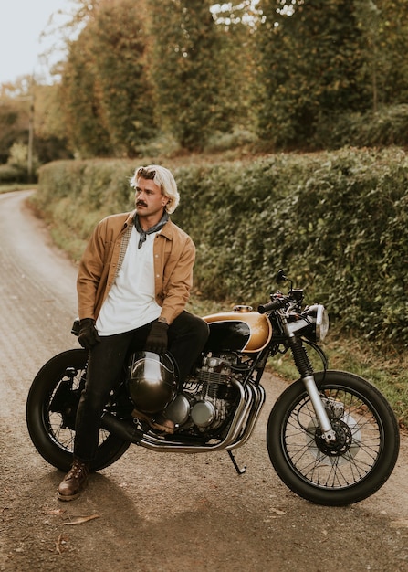 Uomo bello hipster seduto su una moto retrò in campagna