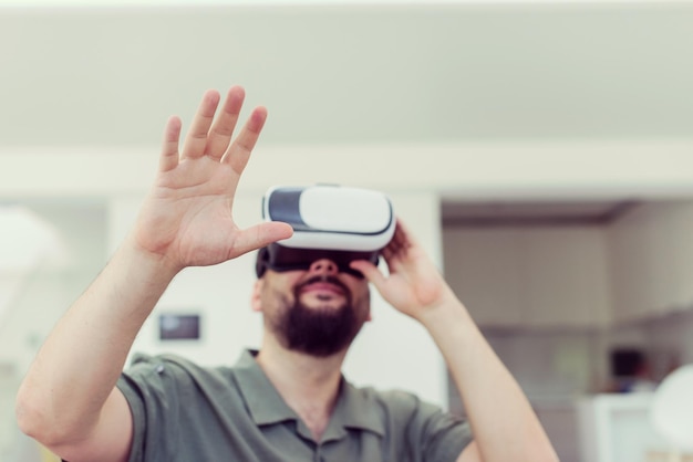Красивый хипстер с бородой примеряет очки виртуальной реальности в современном доме