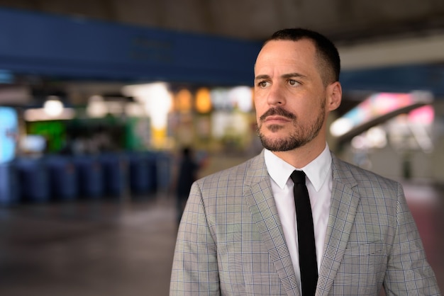 Handsome Hispanic bald bearded businessman walking off at the sky train station