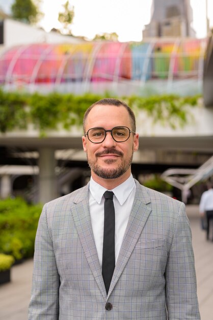 Handsome Hispanic bald bearded businessman with eyeglasses outside modern building