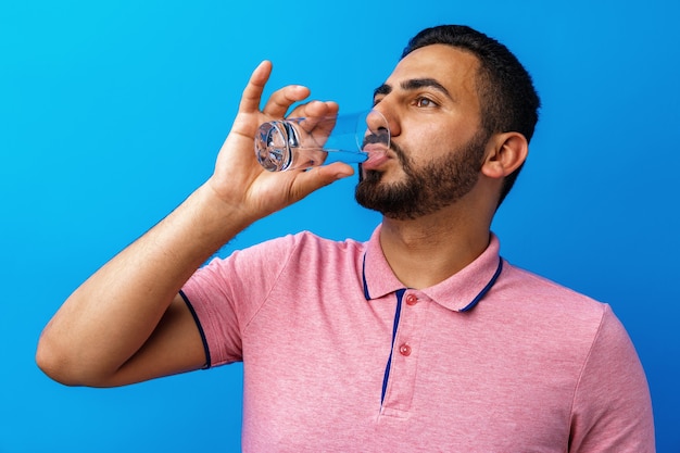 Foto bell'uomo ispanico che beve un bicchiere di acqua fresca su sfondo blu