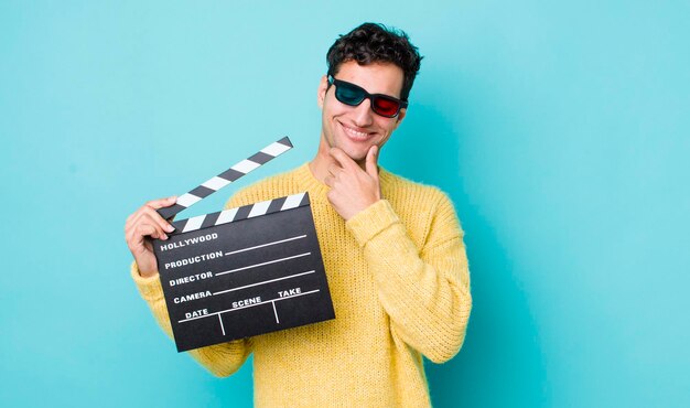 Handsome hispanic man smiling with a happy confident expression with hand on chin cinema concept