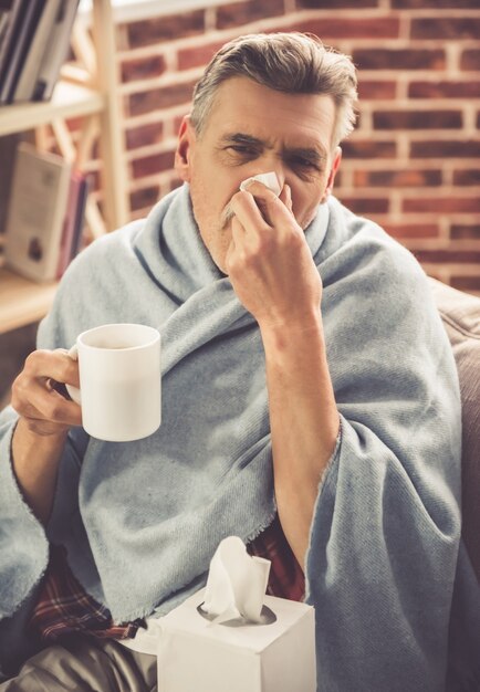 ハンサムな病気の成熟した男は熱いお茶を飲んでいます。