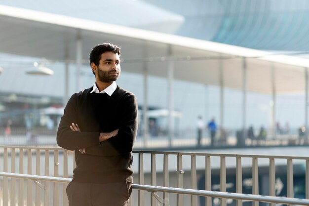 Handsome Indian businessman with arms crossed looking away standing on the street, copy space