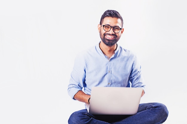 Handsome Indian man sitting and working on laptop over studio white background