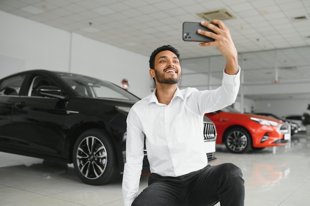 Handsome indian man taking a selfie with car keys to his new automobile at the dealership showroom copyspace technology social media sharing positivity lifestyle travelling tourism