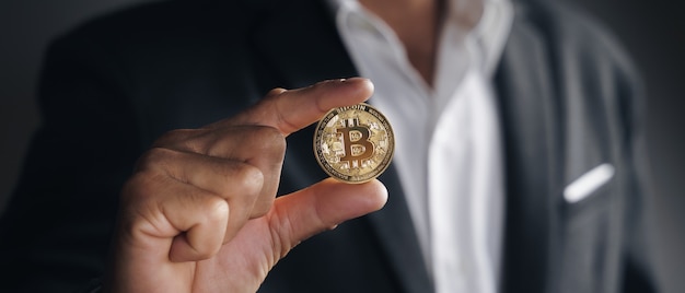 Handsome Investor Businessman in black suit holding a golden bitcoin on dark background, trading, Cryptocurrency, Digital virtual currency, alternative finance and investment Concept.