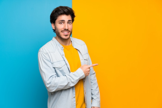 Handsome over isolated colorful background pointing finger to the side