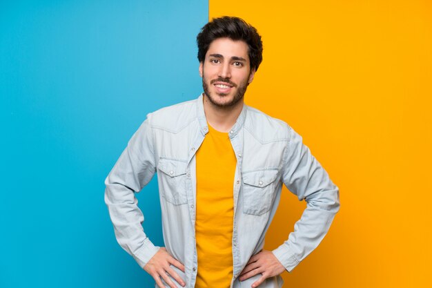 Handsome over isolated colorful background posing with arms at hip and smiling