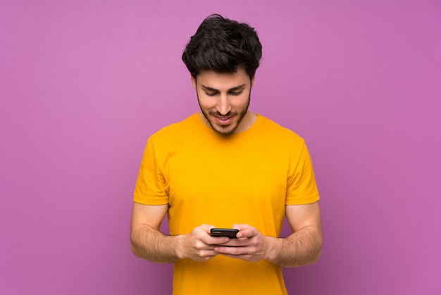 Handsome over isolated purple wall sending a message with the mobile