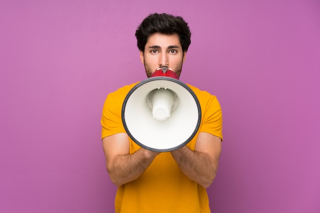 Handsome over isolated purple wall shouting through a megaphone