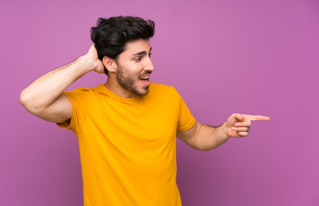 Handsome over isolated purple wall surprised and pointing finger to the side