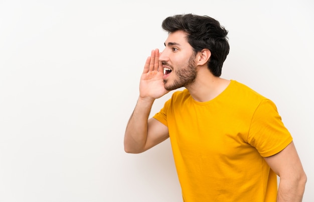 handsome over isolated white wall shouting with mouth wide open