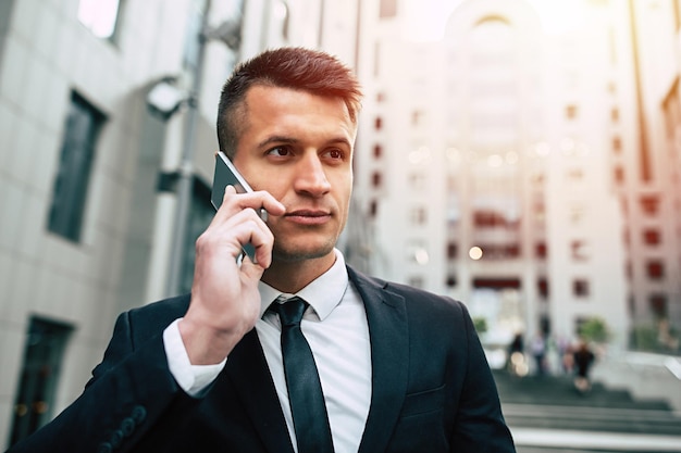 Handsome joyful businessman in smart black suit and tie talking on the phone